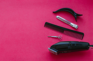 Barbershop. The tools of a professional stylist. Hair clipper, small and large hair clips, comb and hair clip in the form of scissors on a bright pink background. Copy space.
