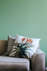 Beige vintage couch with a botanical flower plant print cushion standing in front of a green wall.