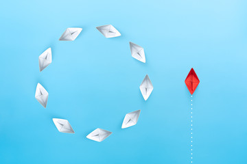 Group of white paper ships float in a circular direction and one red paper ship pointing in different way on blue background. Business for new ideas creativity, innovative and solution concept.