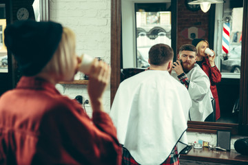 Client during beard shaving in barbershop. Female barber at salon. Gender equality. Woman in the male profession.