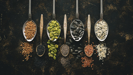A variety of seeds in spoon on dark background. Flat lay, close-up. Chia, flax, pumpkin, sunflower, coriander, sesame, black sesame