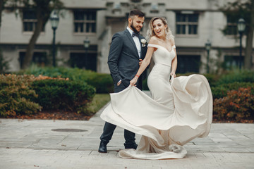 Naklejka premium Beautiful bride in a long white dress. Handsome groom in a black suit. Couple in a summer park