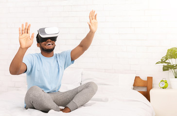 Young cheerful man wearing virtual reality headset in bed