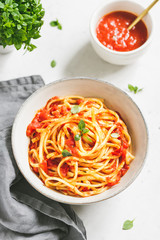 Traditional Italian spaghetti with tomato and Greek basil sauce in a ceramic bowl on a white table.