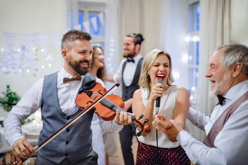 A young bride, groom and other guests dancing and singing on a wedding reception.
