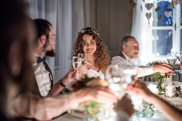 A bride and groom sitting at a table on a wedding, clinking glasses.