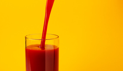 Tomato juice pouring into glass, isolated on yellow color background, with copy space