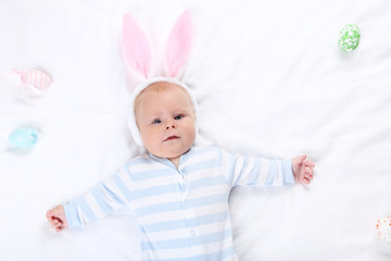 Baby boy in rabbit ears lying on white bed