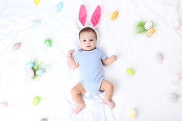 Obraz na płótnie Canvas Cute baby with easter eggs and rabbit ears lying on white bed
