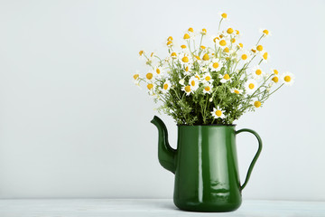 Bouquet of chamomile flowers in jug on grey background