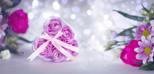 Floral festive background template. A bouquet of flowers and a heart-shaped gift box with rosebuds on a light bokeh background.