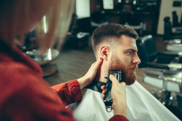 Client during beard shaving in barbershop. Female barber at salon. Gender equality. Woman in the male profession.
