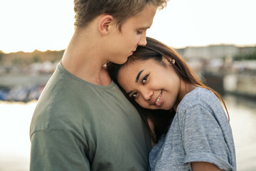 Fototapeta premium Smiling young woman hugging her boyfriend outside by a harbor