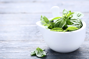 Green basil leafs in mortar on grey wooden table