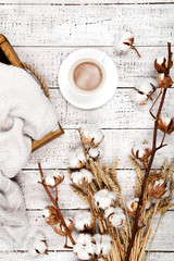 Cotton flowers with cup of cofffee and sweater on white wooden table