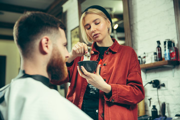 Client during beard shaving in barbershop. Female barber at salon. Gender equality. Woman in the male profession.