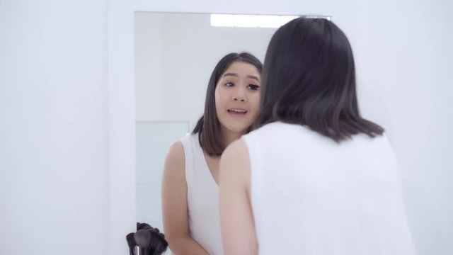 Beautiful Asian woman using eyelash curler makeup in front mirror, Happy female using beauty cosmetics to improve herself ready to working in bedroom at home. Lifestyle women relax at home concept.