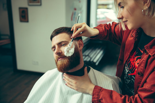 Client during beard shaving in barbershop. Female barber at salon. Gender equality. Woman in the male profession.