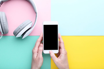 Smartphone in female hands with headphones on colorful background