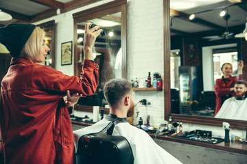 Client during beard shaving in barbershop. Female barber at salon. Gender equality. Woman in the male profession.
