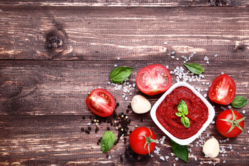 Ketchup in bowl with spices and garlic on brown wooden table