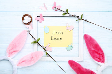 Rabbit ears with small eggs, tree branches and text Happy Easter on wooden table