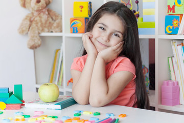 School activity, happiness and smartness.  Cute adorable child girl sitting by the table and smiling.