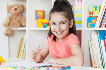 School activity, happiness and smartness.  Cute adorable child girl sitting by the table and smiling.