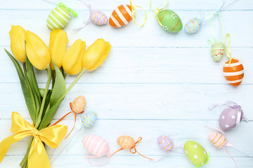 Yellow tulips with colorful easter eggs on wooden table