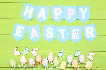 Small rabbits with eggs and text Happy Easter on green wooden table