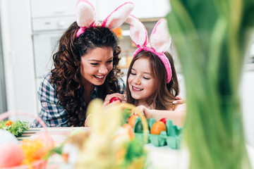 A mother and her cute daughter are painting colorful eggs and wearing bunny ears. Happy family are preparing for Easter.