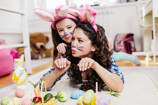 Mother and her cute little daughter playing in children's room while preparing Easter decoration.