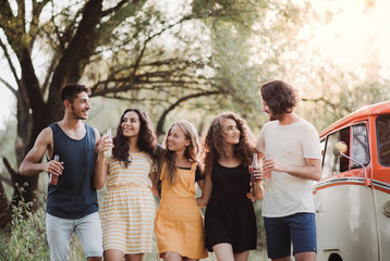 A group of young friends on a roadtrip through countryside, holding bottles and walking.
