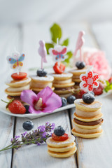 Fruit, berry and pancake canapes on white wooden table