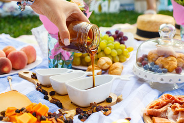 Woman hand pours honey from transparent bottle to sauceboat, at summer picnic background