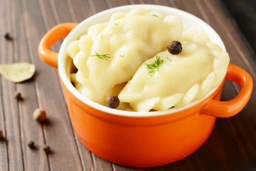 Dumplings with potatoes with herbs, spices and butter in a ceramic portion pot on a dark background. Varenyky, vareniki, pierogi, pyrohy - dumplings with filling.