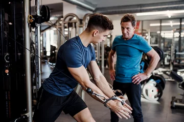  A senior man with a young trainer doing strength workout exercise in gym. © Halfpoint
