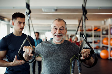 A group of cheerful seniors in gym with a young trainer doing exercise with TRX.