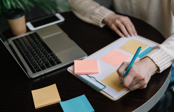 Closeup shot of university student hand holding pen and writing information on sticky note, exam preparation, learning language. Woman freelancer working from home, using scrum for productivity 
