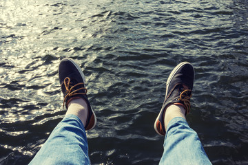 Male feet in black sneakers over the surface of the water.