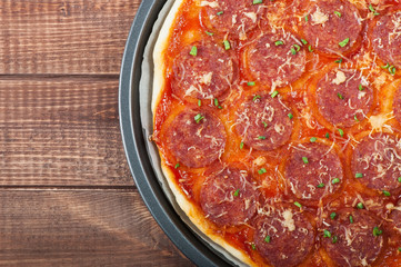 Pizza with salami and cheese on the old wooden background.