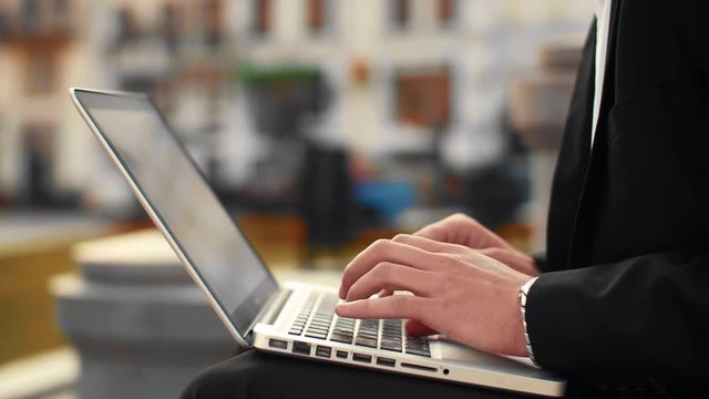 Close up shot of male hands typing on laptop keyboard with city street on the background. Businessman hands typing 