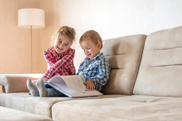 Cute little brother and sister reading book together at home