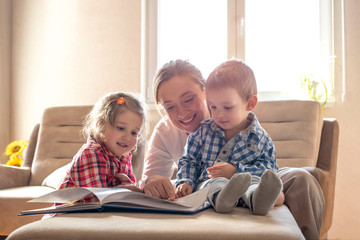 Obraz premium Mother and children reading book and having fun while spending time together at home