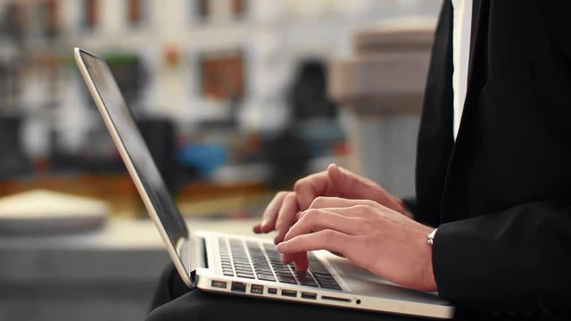 Close up shot of male hands typing on laptop keyboard with city street on the background. Businessman typing out of office