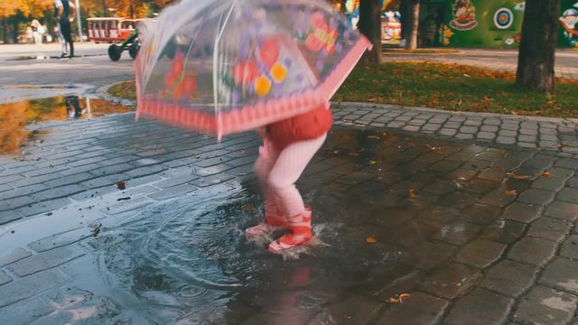 Girl in Rubber Boots Jumping on Puddle with Umbrella
