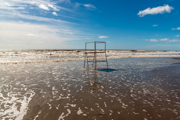 Empty beach in Argentina with high tide with a red lifeguard stand made of tubes with some clouds