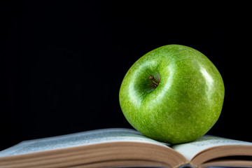 Open book and a green apple in front of black background - Powered by Adobe