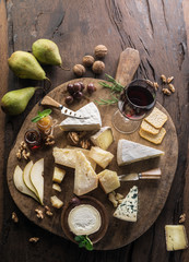 Cheese platter with organic cheeses, fruits, nuts and wine on wooden background. Top view. Tasty cheese starter.