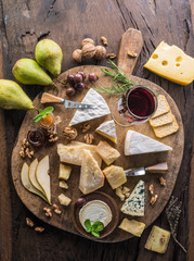 Cheese platter with organic cheeses, fruits, nuts and wine on wooden background. Top view. Tasty cheese starter.